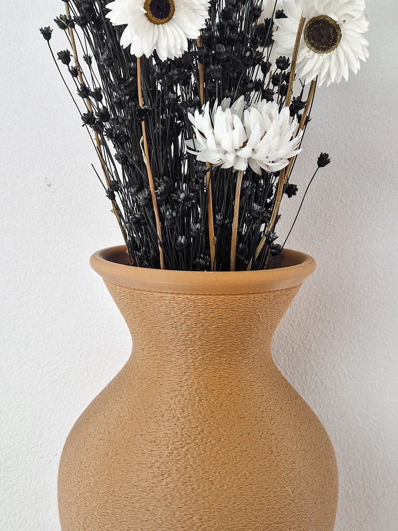 May include: A brown ceramic vase with a textured surface holds a bouquet of white dried flowers with black stems.