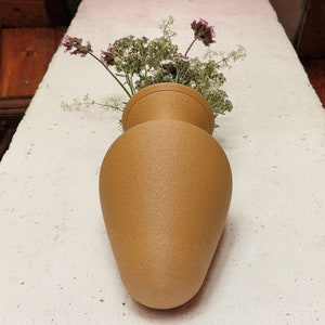 May include: A tan ceramic vase with a textured surface, filled with a bouquet of small white and purple flowers.