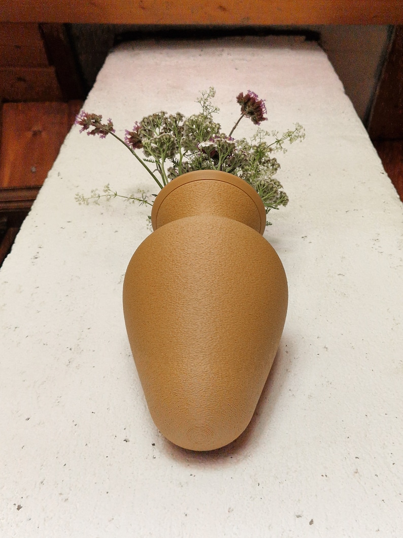 May include: A tan ceramic vase with a textured surface, filled with a bouquet of small white and purple flowers.