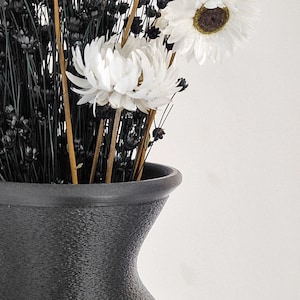 May include: A black ceramic vase with a textured surface holds a bouquet of dried white flowers and black dried grasses.