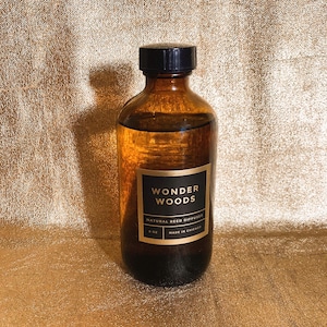 May include: A brown glass bottle with a black cap, labeled "WONDER WOODS NATURAL REED DIFFUSER." The bottle contains a clear liquid and is 8 oz. Made in Chicago.