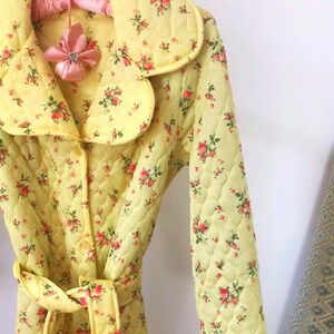 May include: A yellow quilted robe with a floral print and a tie belt. The robe has a collar and long sleeves.