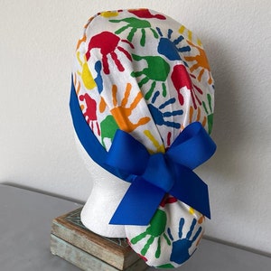 May include: A white scrub hat with a colorful handprint pattern and a blue ribbon tied in a bow at the back.