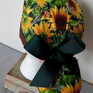 May include: A green, brown, and yellow surgical scrub hat with a sunflower print and a dark green bow.