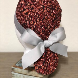 May include: A brown and black scrub hat with a coffee bean pattern and a gray ribbon tied in a bow at the back.
