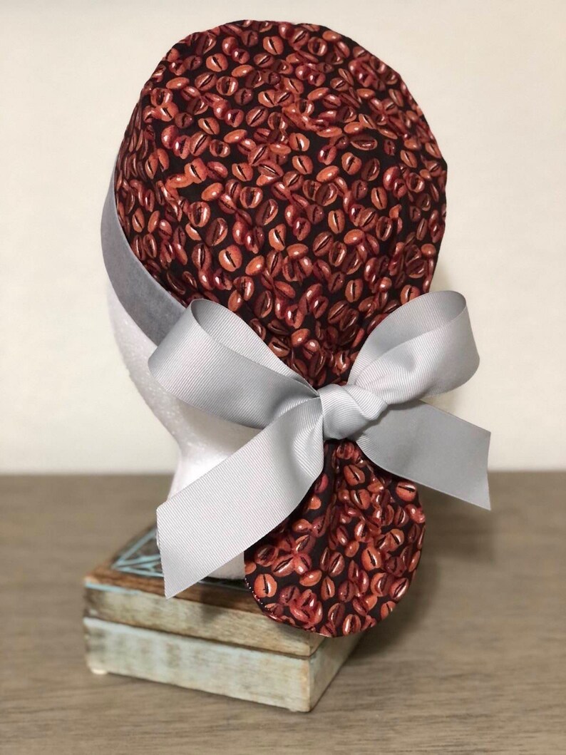 May include: A brown and black scrub hat with a coffee bean pattern and a gray ribbon tied in a bow at the back.