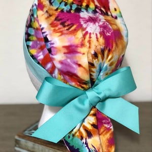 May include: A colorful tie-dye surgical scrub hat with a turquoise ribbon tied in a bow at the back.