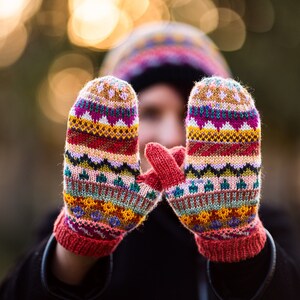 Könnte beinhalten: Ein Paar bunte Strickhandschuhe mit geometrischem Muster. Die Handschuhe sind rot, gelb, grün, blau und pink.