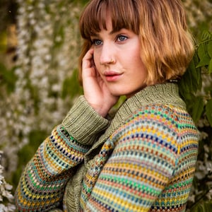 Könnte beinhalten: Ein mehrfarbiger Strickcardigan mit grünem Kragen und Manschetten. Der Cardigan hat ein Muster aus horizontalen Streifen in verschiedenen Farben, darunter Grün, Gelb, Blau und Braun. Das Model trägt den Cardigan.