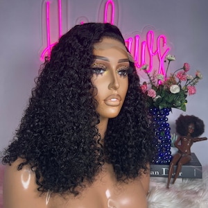 May include: A black curly human hair wig on a mannequin head. The wig is styled in a short bob with loose curls.