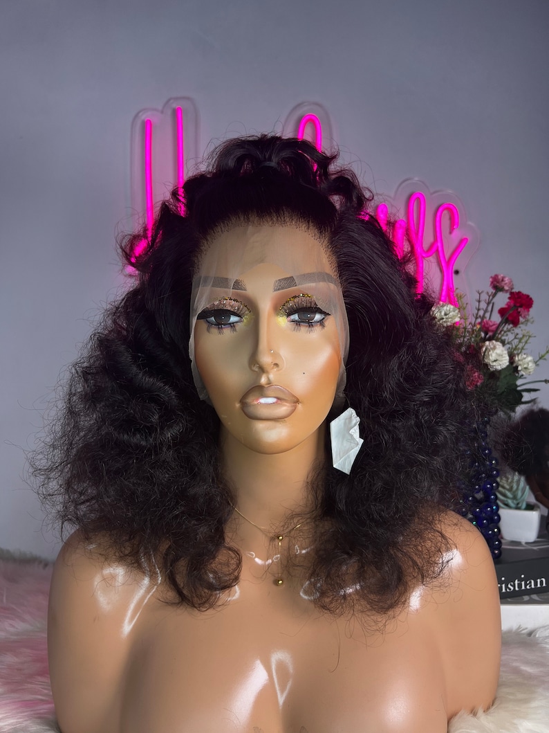 May include: A black curly human hair wig on a mannequin head. The wig has a lace front and is styled in a voluminous, curly look.