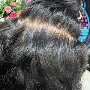 May include: A black human hair wig with a lace closure. The wig is styled in a bun and the lace closure is visible.