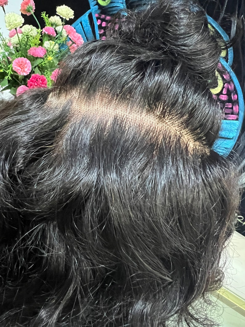 May include: A black human hair wig with a lace closure. The wig is styled in a bun and the lace closure is visible.