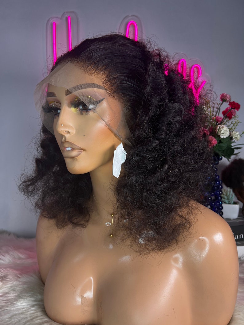May include: A black curly human hair wig on a mannequin head. The wig has a lace front and is styled in a short, voluminous curly style.