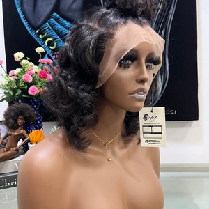 May include: A dark brown wig with a lace front and a wavy texture. The wig is styled with a high ponytail and is displayed on a mannequin head. The mannequin is wearing a gold necklace.