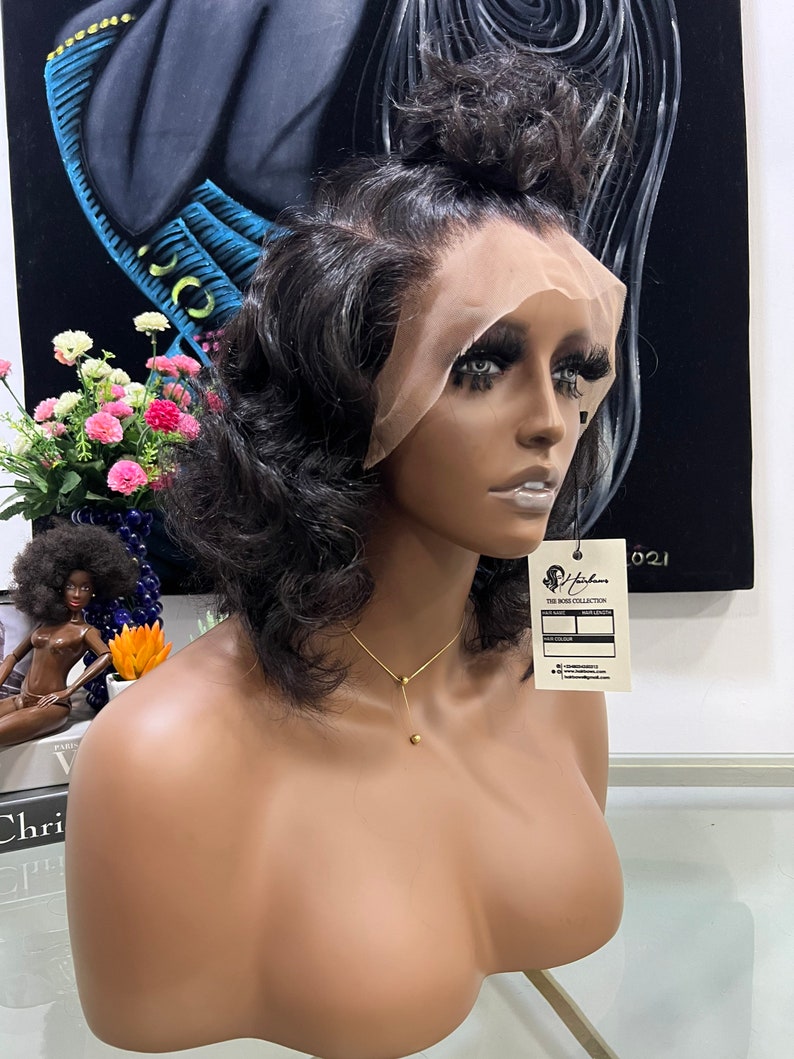 May include: A dark brown wig with a lace front and a wavy texture. The wig is styled with a high ponytail and is displayed on a mannequin head. The mannequin is wearing a gold necklace.