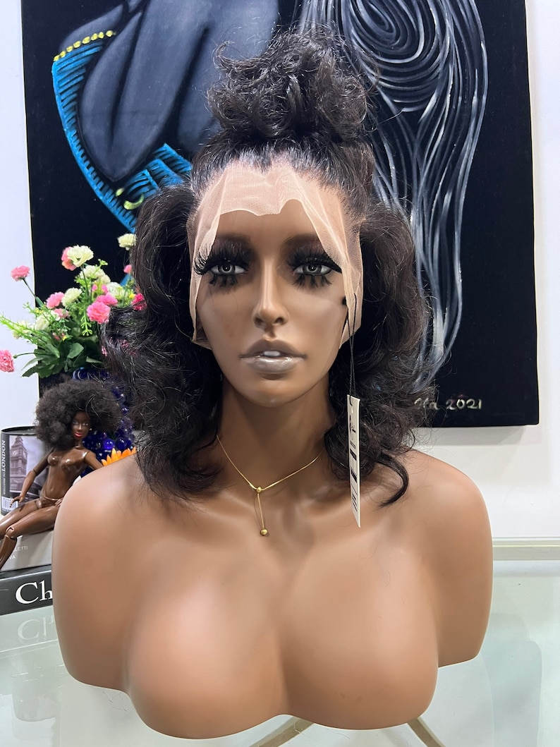 May include: A dark brown human hair wig with a lace front and a high ponytail. The wig is on a mannequin head with a light brown skin tone. The mannequin is wearing a gold necklace.