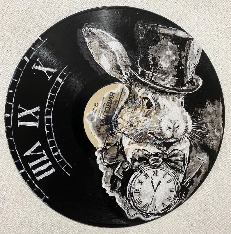 K&ouml;nnte beinhalten: Schwarze Vinyl-Schallplatte mit einem wei&szlig;en Hasen in Zylinder und Anzug, der eine Taschenuhr h&auml;lt. Der Rand der Schallplatte hat ein Zifferblatt-Design mit r&ouml;mischen Ziffern. Der Hase ist in Graustufen gemalt.