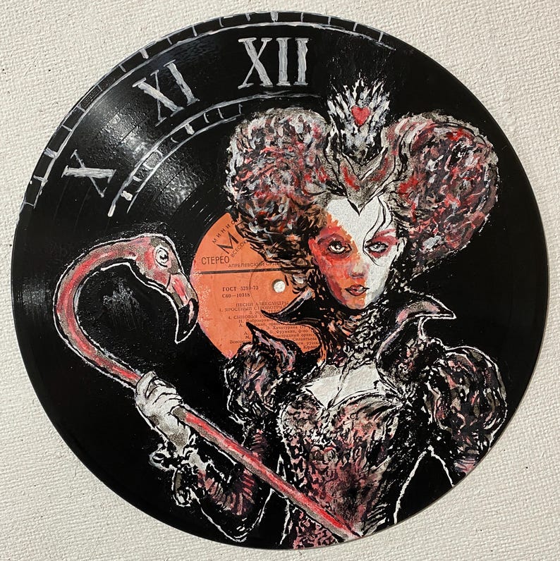 K&ouml;nnte beinhalten: Eine schwarze Schallplatte, bemalt mit dem Portr&auml;t einer K&ouml;nigin, die eine Krone tr&auml;gt und einen rosa Flamingo h&auml;lt. Der Hintergrund zeigt wei&szlig;e r&ouml;mische Ziffern f&uuml;r elf und zw&ouml;lf, die ein Zifferblatt auf der Platte bilden.