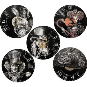 K&ouml;nnte beinhalten: F&uuml;nf runde Wanduhren aus schwarzen Schallplatten, jede mit handgemalten Illustrationen von Figuren, darunter ein Kaninchen mit Taschenuhr, eine K&ouml;nigin mit Flamingo, eine Person mit Zylinder, ein Hutmacher und eine Katze.