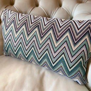 Peut inclure: Un coussin décoratif avec un motif en chevron dans des tons de bleu, vert, blanc et gris. Le coussin est fait d'un tissu doux et texturé et est parfait pour ajouter une touche de style à n'importe quelle pièce.