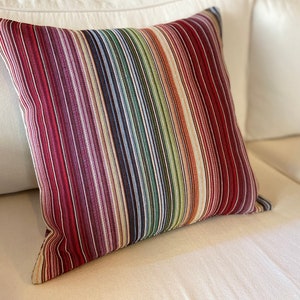 May include: A striped throw pillow with a variety of colors, including red, purple, green, and blue. The pillow is made of a soft, woven fabric.