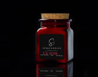 May include: A red glass jar with a cork lid. The jar has a black label with the text "SEX & CANDLES" and "CE SOIR". The candle is hand-poured and made with a soy blend. The jar is reflected on a black surface.