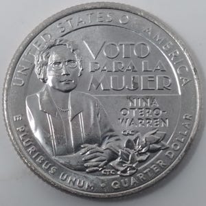 May include: A silver quarter dollar coin featuring a portrait of Nina Otero-Warren, with the text "VOTO PARA LA MUJER" and "Nina Otero-Warren". The coin also includes the inscriptions "United States of America", "E Pluribus Unum", and "Quarter Dollar".