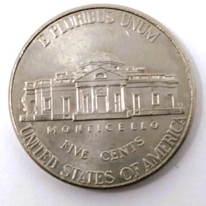 Può includere: Una moneta di nichel d'argento degli Stati Uniti. La moneta presenta le parole "E PLURIBUS UNUM" in alto e "UNITED STATES OF AMERICA" in basso. La moneta presenta anche le parole "MONTICELLO" e "FIVE CENTS".