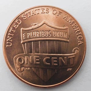 May include: A close-up of a copper-colored United States one-cent coin. The coin features the words "UNITED STATES OF AMERICA" and "ONE CENT". The phrase "E PLURIBUS UNUM" is also visible.