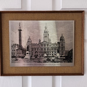 Op de afbeelding: Een ingelijst zilverkleurig drukwerk van de Municipal Buildings, George Square, Glasgow, Schotland. De print is geplaatst op een bruine jute achtergrond.