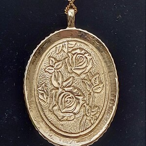 May include: A gold-tone pendant necklace with a detailed oval-shaped charm featuring an embossed design of three roses.
