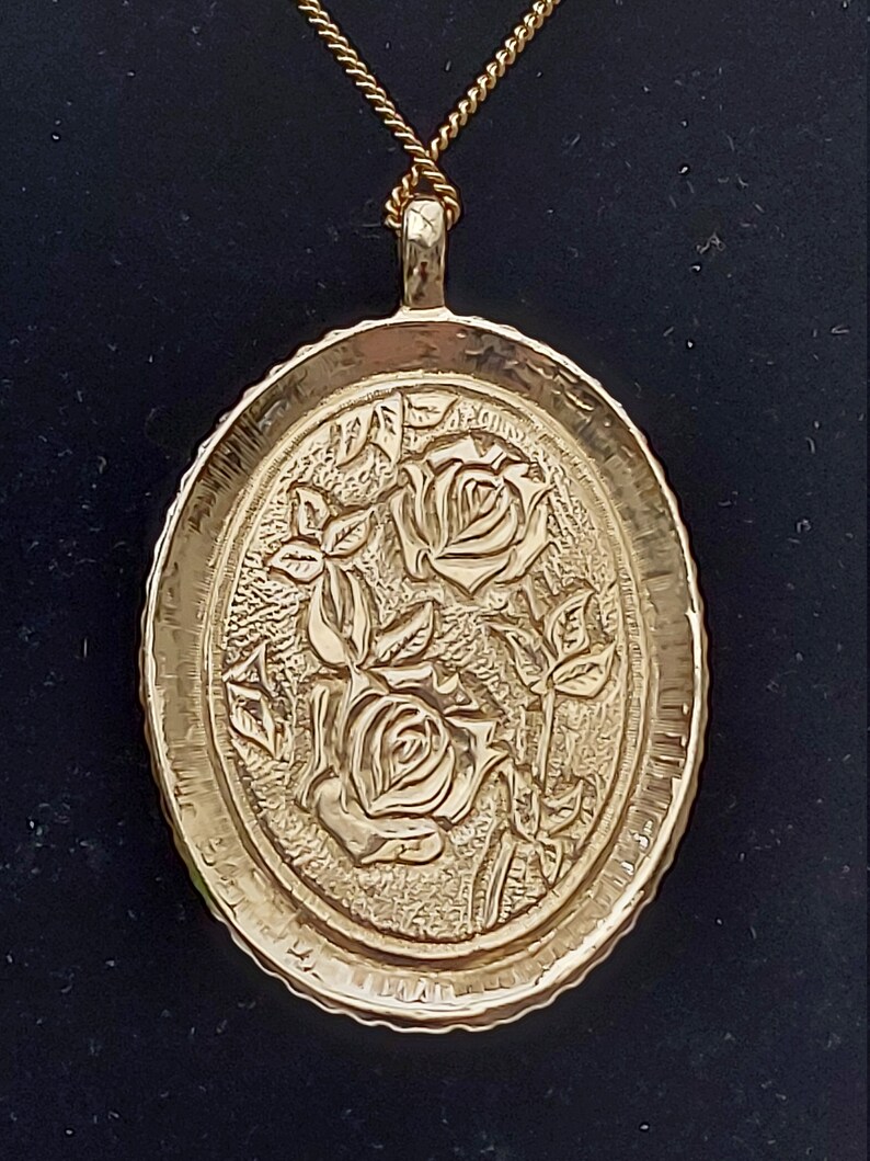 May include: A gold-tone pendant necklace with a detailed oval-shaped charm featuring an embossed design of three roses.