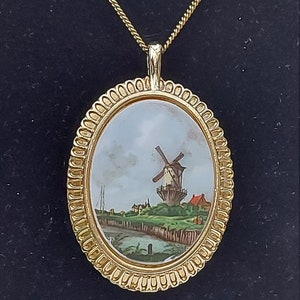 May include: A gold oval pendant necklace with a detailed, ornate frame. The pendant features a painted scene of a windmill in a landscape.