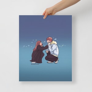 May include: A print featuring an illustration of a couple in a tender moment. The woman, with long brown hair, is touching the man's face, who is wearing a blue and yellow hoodie. The background is a gradient of blue.