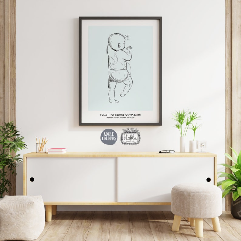 Op de afbeelding: Een zwart ingelijste poster met een lichtblauwe achtergrond en een lijntekening van een baby in een luier. De poster zegt "Schaal 1:1 van George Joshua Smith" onderaan.