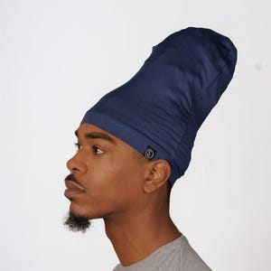 Könnte beinhalten: Eine dunkelblaue Satin-Schlafhaube mit einem kleinen schwarzen Logo an der Seite. Die Haube wird von einer Person mit brauner Haut getragen.