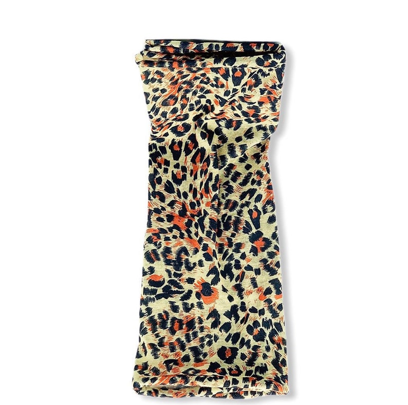 May include: A beige fabric scarf with a leopard print pattern in shades of orange, black, and brown.