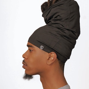 Peut inclure: Un bonnet de nuit en satin noir avec un petit logo sur le côté. Le bonnet est porté par une personne avec des dreadlocks.