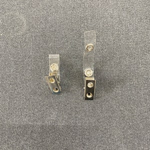 May include: Two clear plastic badge holders with metal clips. The clips have two holes each.