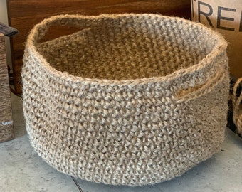 May include: A large, brown, crocheted basket with a single handle. The basket is made of natural fibers and has a woven texture.
