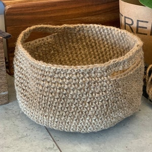 Peut inclure: Un grand panier en crochet brun avec une seule poignée. Le panier est fait de fibres naturelles et a une texture tissée.