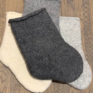 May include: Three knitted stockings in different colors: white, gray, and dark gray. The stockings are made of a soft, fuzzy material and are perfect for hanging on a fireplace mantel or decorating a Christmas tree.