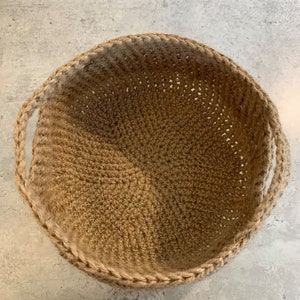 May include: A round, tan, crocheted basket with two handles. The basket is made of natural fibers and has a woven texture.