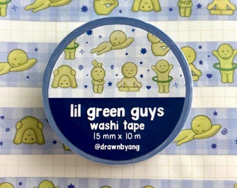 Puede incluir: Un rollo de cinta washi con un patrón de cuadros azul claro y blanco, decorado con pequeñas figuras verdes de dibujos animados en varias poses, estrellas y corazones. La etiqueta dice lil green guys washi tape 15 mm x 10 m @drawnbyang.