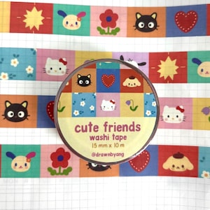 May include: A roll of washi tape labeled cute friends 15 mm x 10 m @drawnbyang. The tape features a grid pattern with colorful squares containing illustrations of a white cat, a black cat, a heart, a flower, a sun, and a puppy on a grid background.