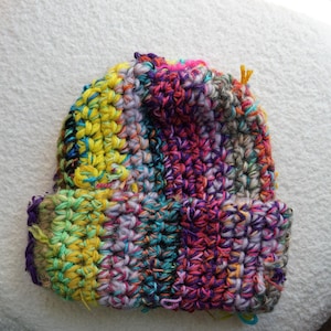 May include: A colorful, handmade crochet beanie hat. The hat features a vibrant mix of colors including yellow, pink, purple, blue, and green. The brim is folded up, and the hat appears to be made of a soft, textured yarn.