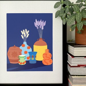 Peut inclure: Une impression encadrée d'une nature morte représentant divers vases et pots en céramique colorés avec des fleurs séchées sur un fond bleu foncé.