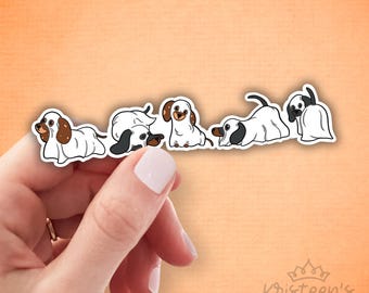 May include: A sticker sheet with five dachshund dog illustrations. The dogs have white bodies with brown or black markings, in different poses. One dog is dressed as a ghost. The background is a light orange.