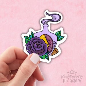 May include: A sticker featuring a purple potion bottle with a yellow and stitched object inside, emitting purple smoke. A purple rose and green leaves surround the bottle. The sticker has a white border and the text "kristeen's kingdom".